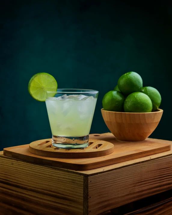limes and a wooden bowl on top of a table