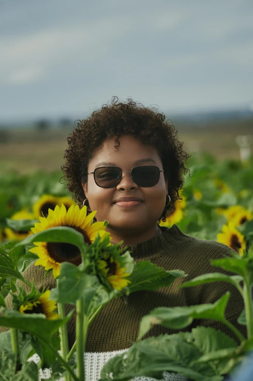 an african american woman poses in front of a large sunflower