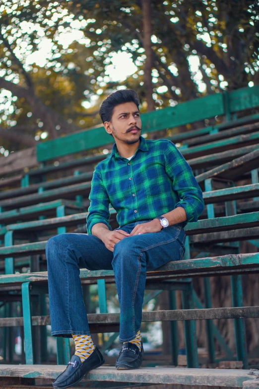 a man wearing blue and green clothing sitting on a fence