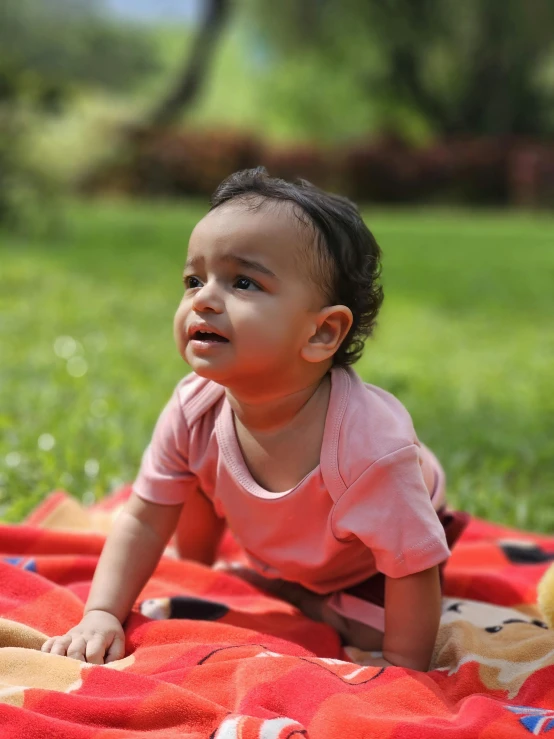 a baby girl laying on a blanket on the grass