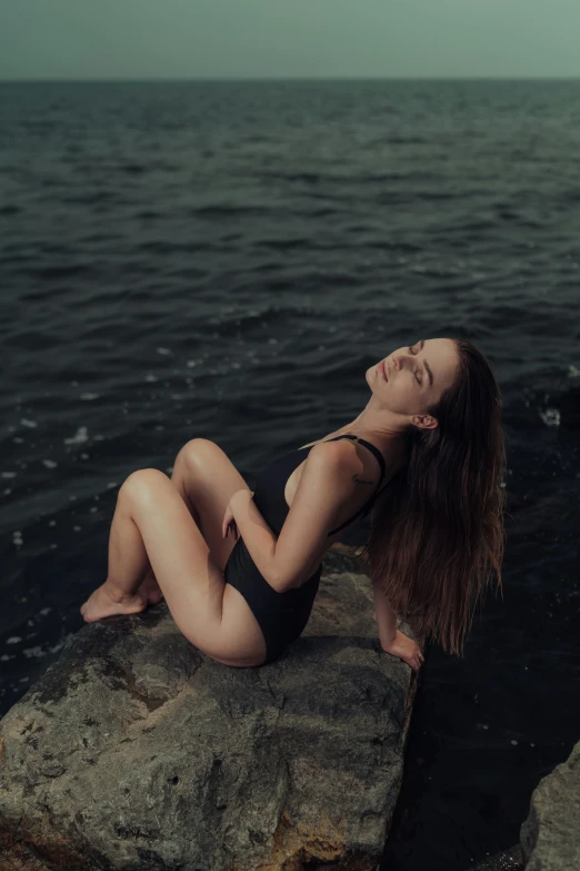 a woman in a bathing suit sits on a rock next to the ocean