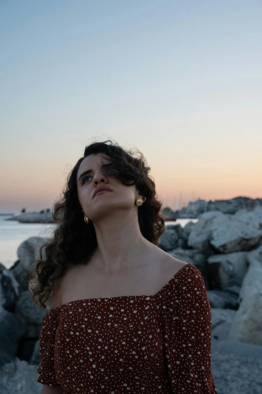 a woman in red dress standing on beach with water and rocks