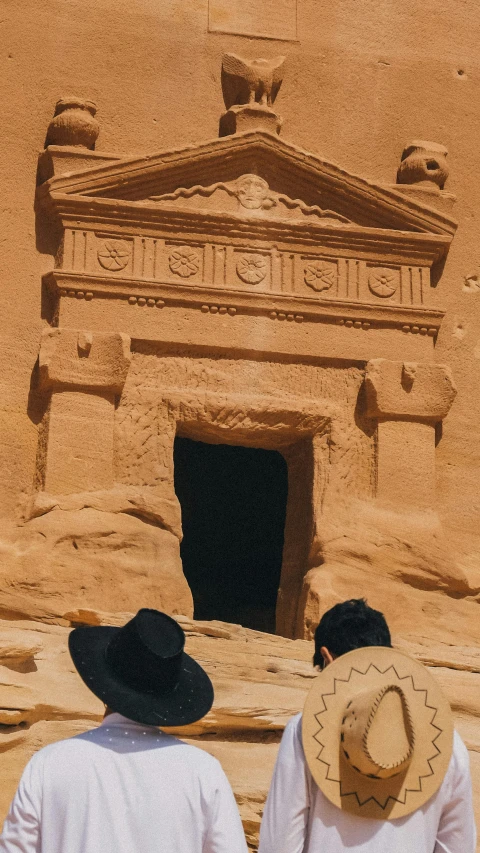 two people in front of a building with a cave entrance