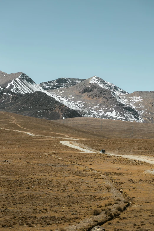 some snow covered mountains a dirt road and some cars