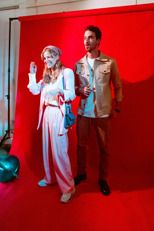 two people posing together in front of red wall