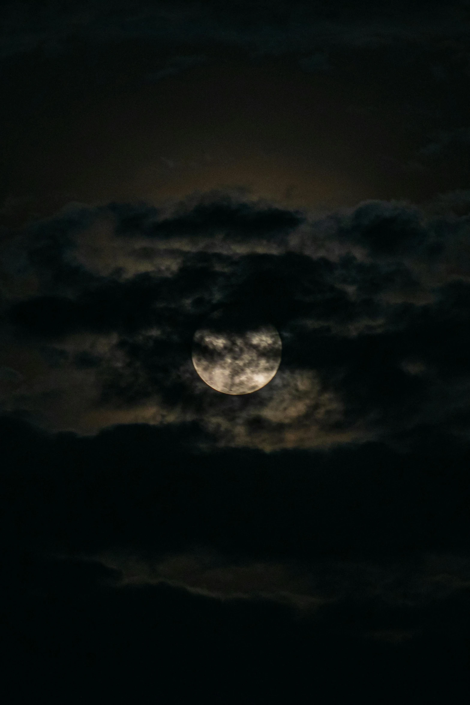 the moon rising behind dark clouds with a black sky