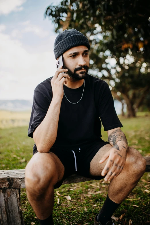 a man sitting on a bench in a field talking on the phone