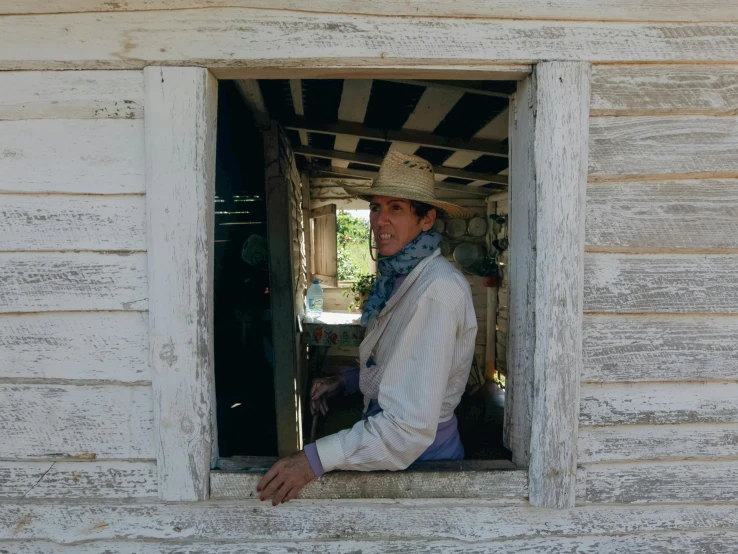 a person wearing a hat and white coat sitting in a window sill