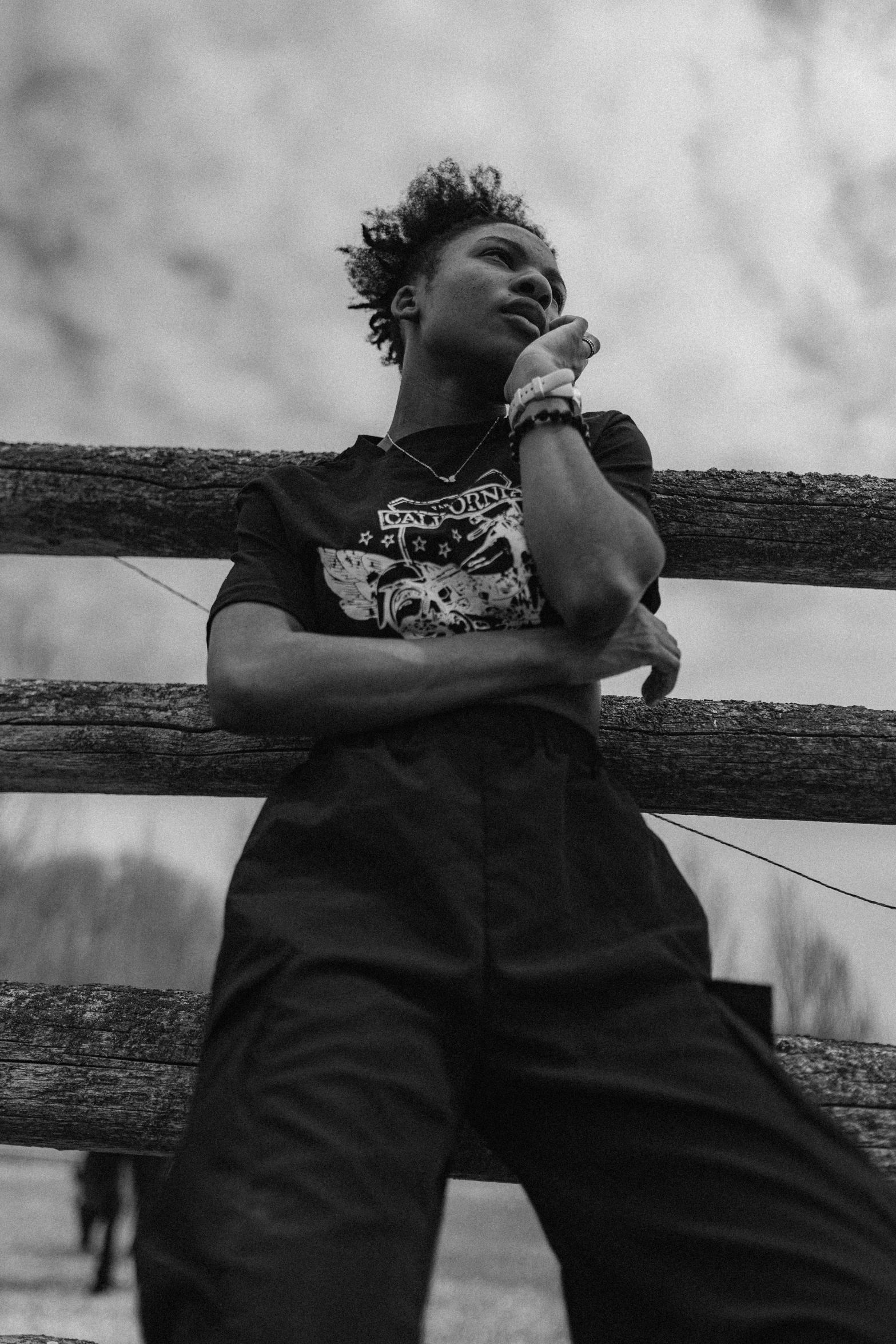 black and white image of young man sitting on fence