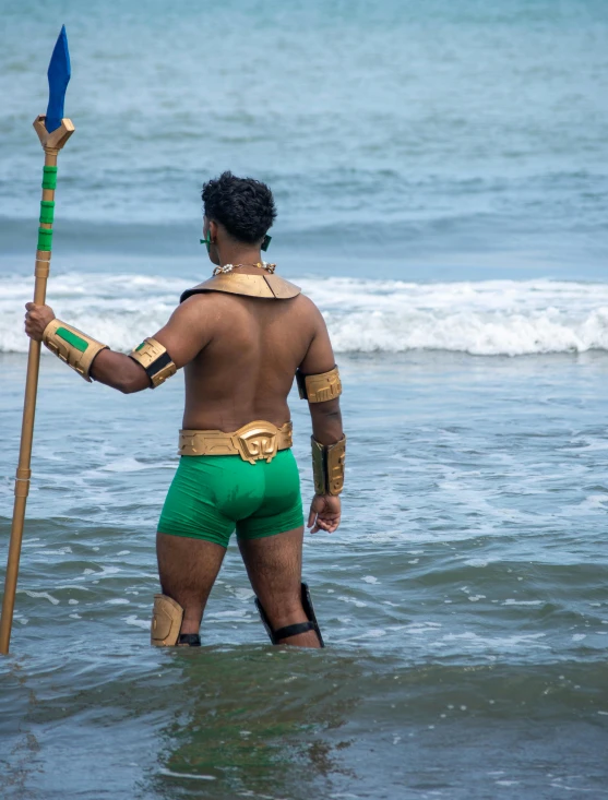 a man with spear, in green shorts, standing in the water