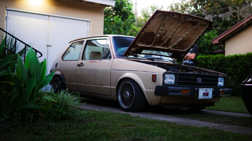 a dirty, brown car with a hood open parked on the side of the road