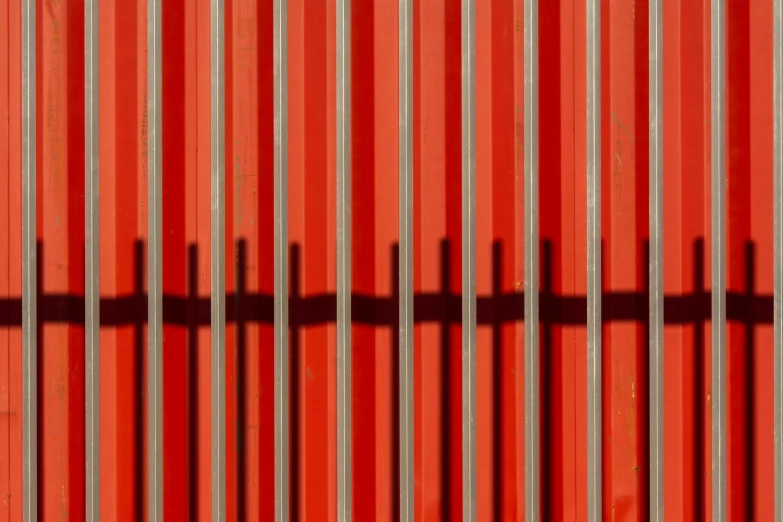 red and silver bars and fence casting shadows on them