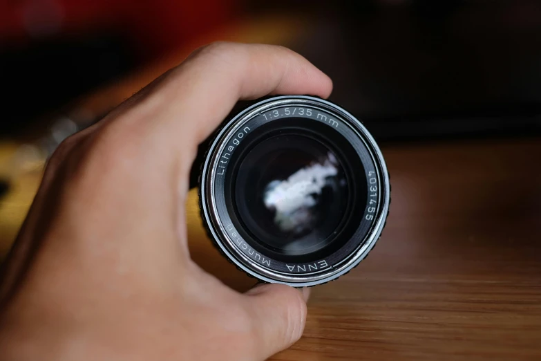 a person's hand holding a camera lens on a table