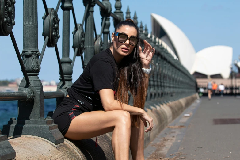 a woman sitting on a railing in front of the sydney opera