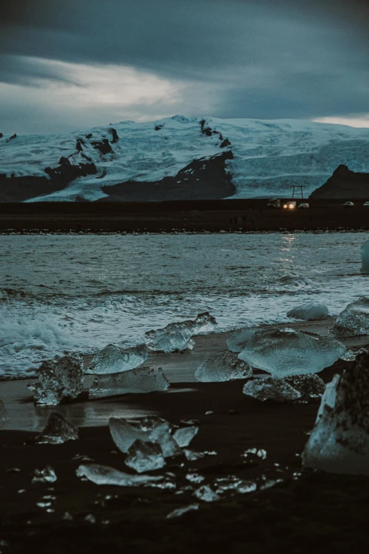 iceberg on an empty beach, with the snow capped mountains in the background