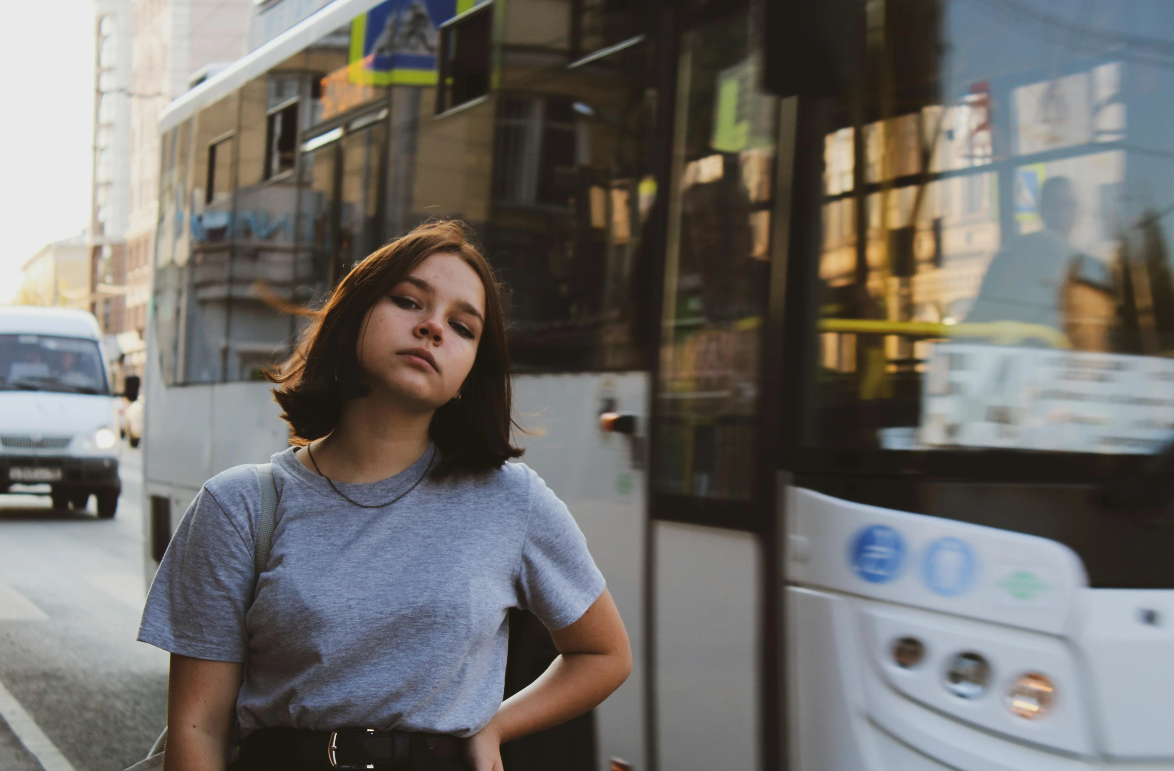 woman in grey shirt standing outside a city bus