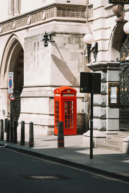 a red phone box sits beside a sign in front of a building