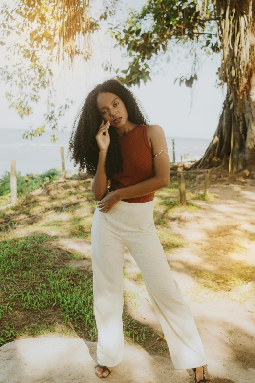 a woman posing outside in front of a tree talking on her cell phone