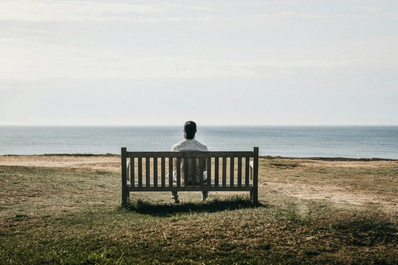 a man is sitting alone on the bench next to the ocean