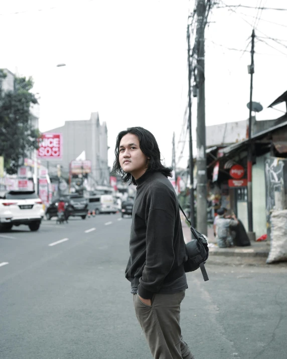 the girl with long hair looks to the side while standing on the street