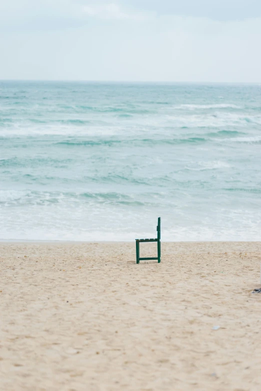 a lone chair sitting on the beach next to the ocean