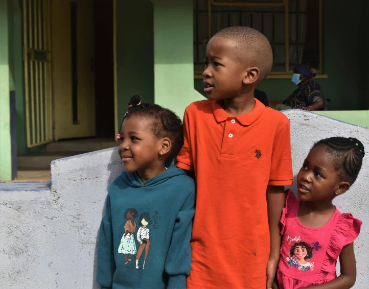 three children standing next to each other near a wall