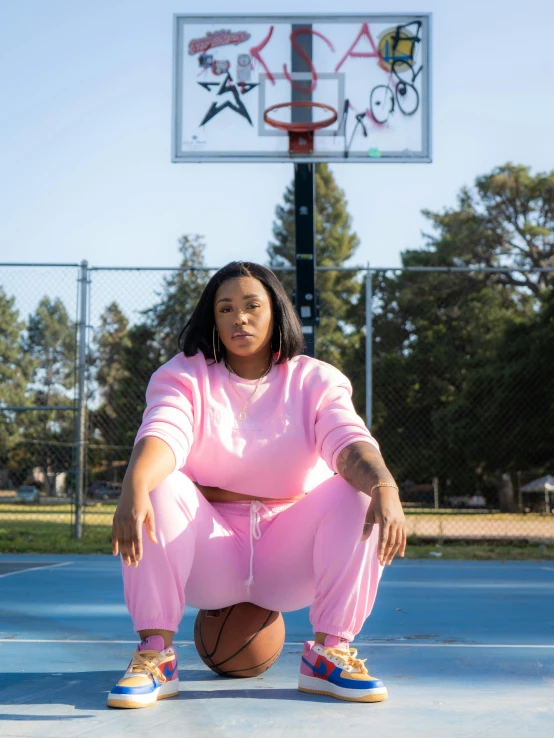 young woman in pink suit kneeling down by basketball hoop