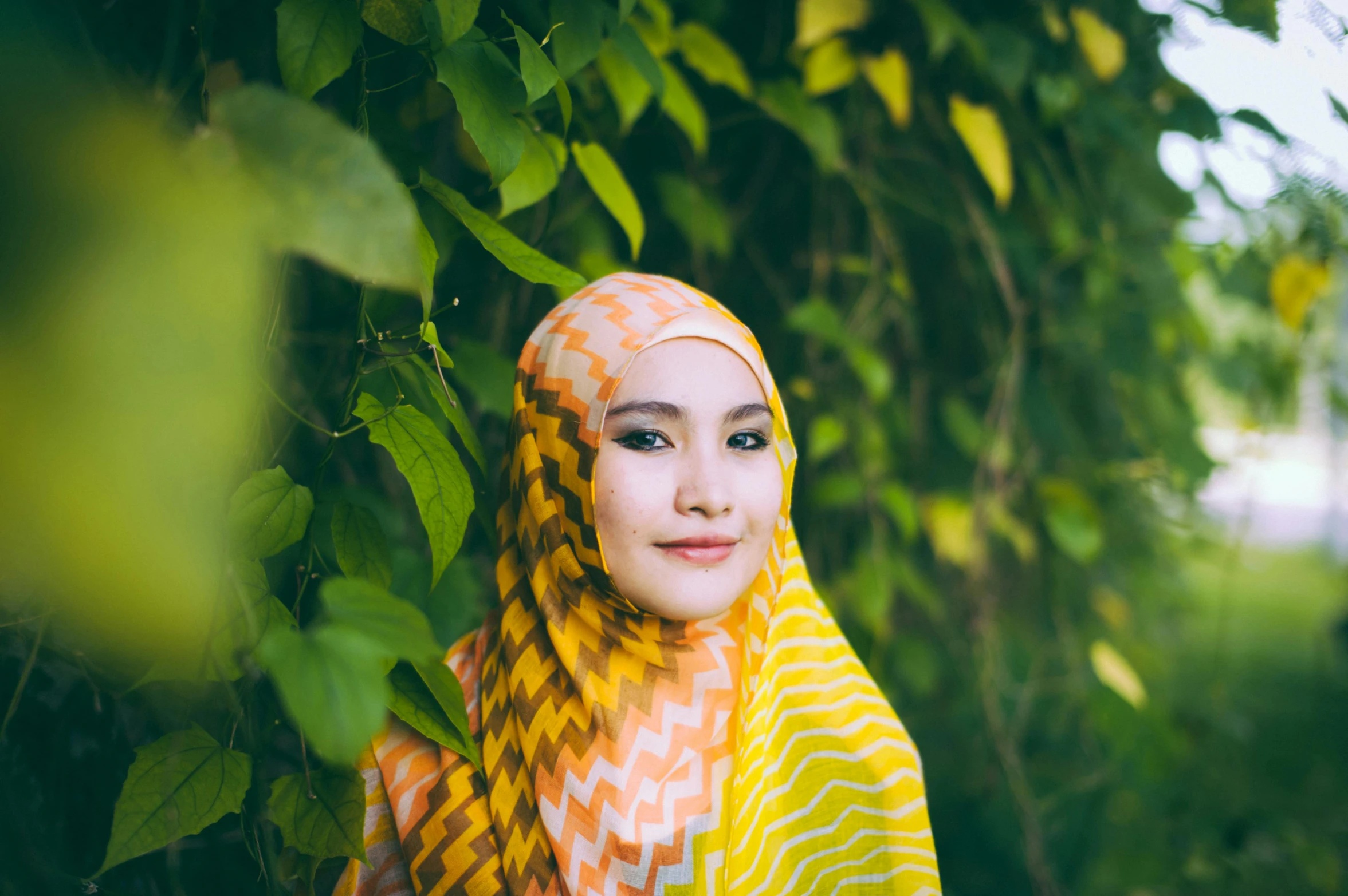 young woman with head scarf smiling in front of a tree