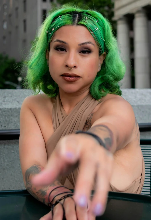 a woman with green hair and a brown dress pointing to the camera