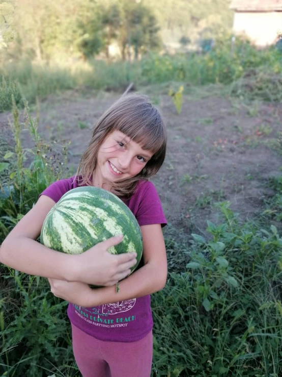 a little girl holding a watermelon in the middle of a field