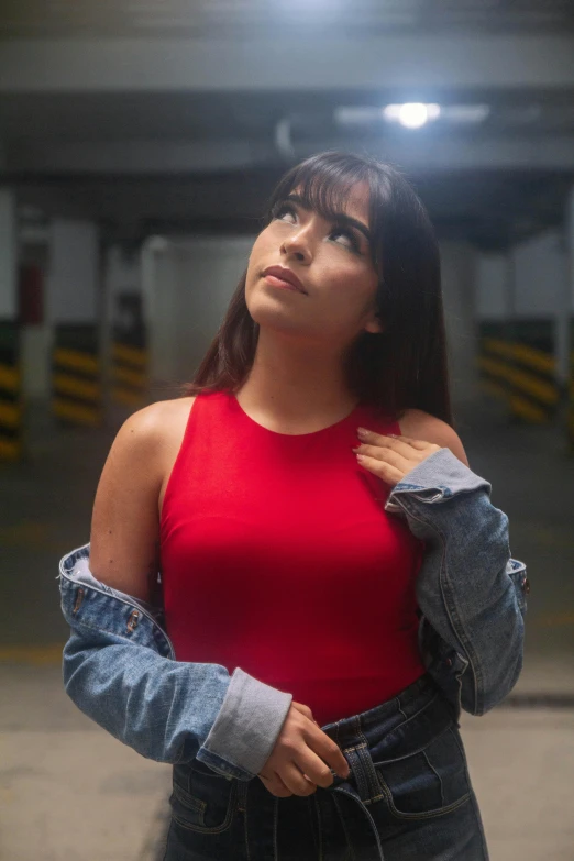 a woman in a red tank top and denim jacket looking up