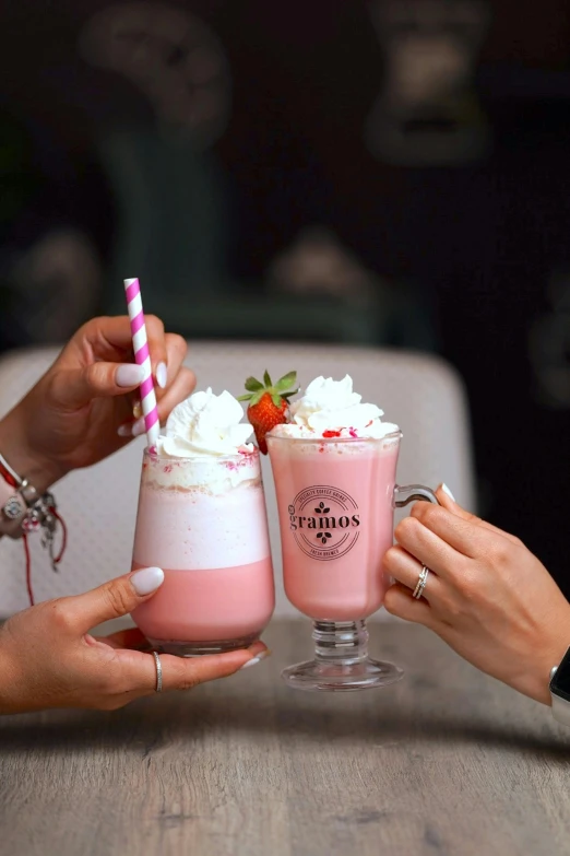 two people holding cups with milkshakes and strawberries