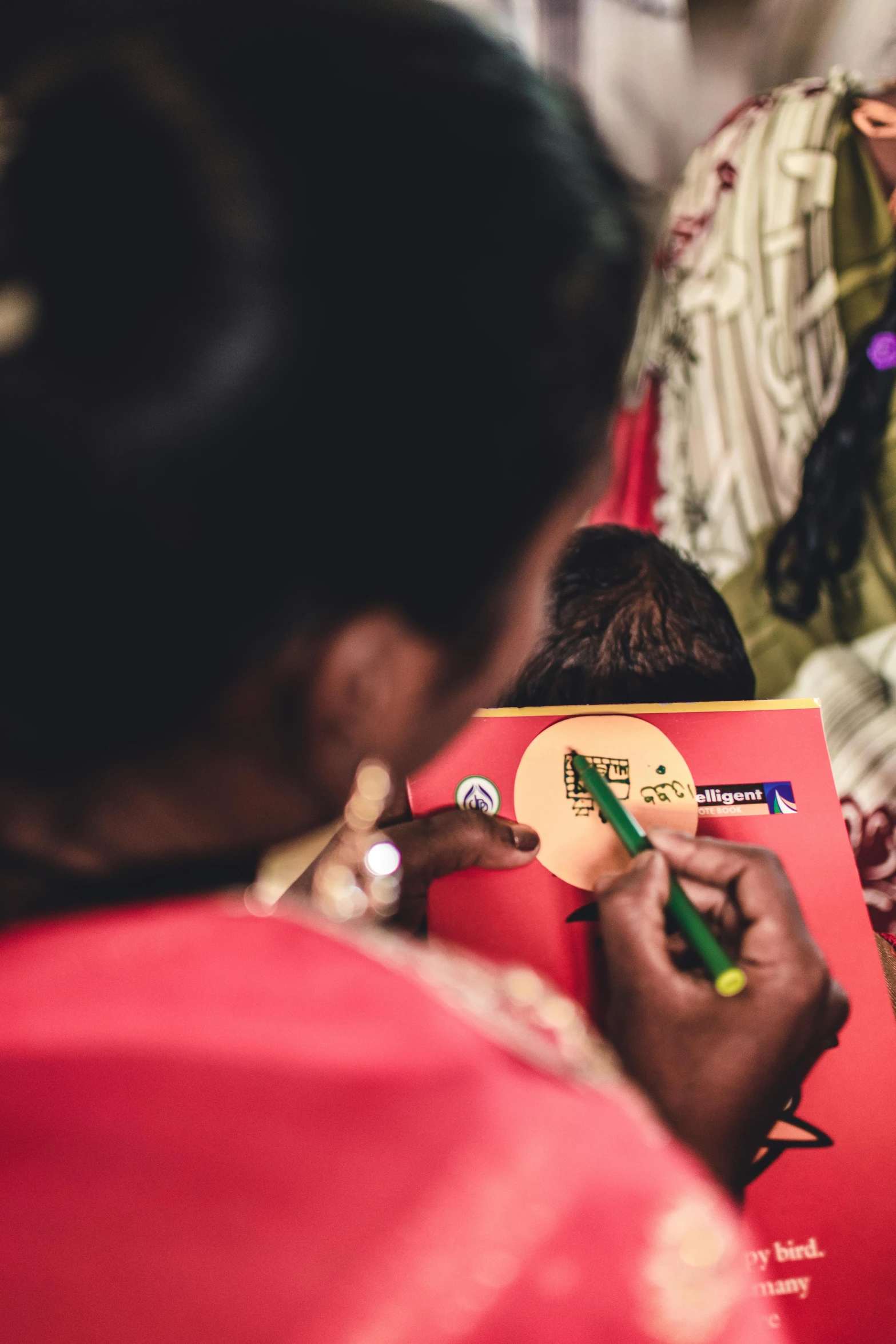 a woman writing on a red notebook with pencil