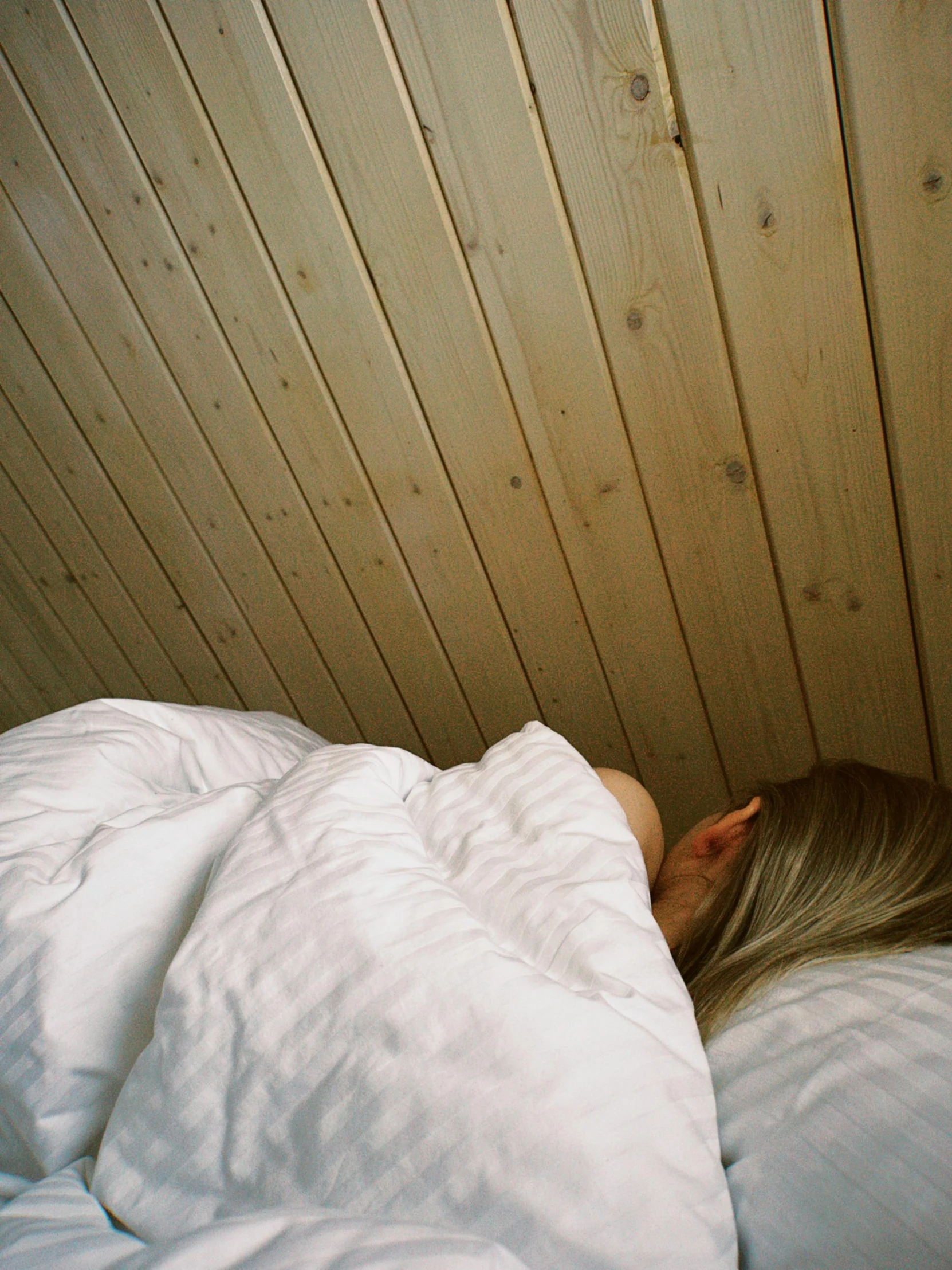 a woman lying in a bed under a wooden head board