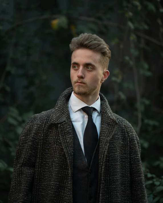 a man in jacket and tie in front of some trees