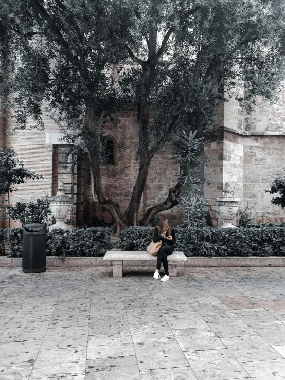 a person sitting on a bench in a courtyard with a brick building