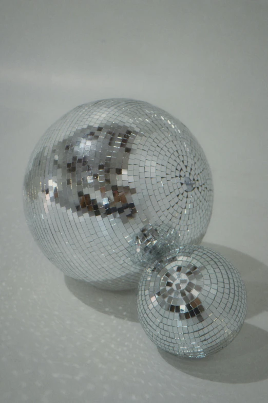 two disco ball stand on a table with its reflection on it