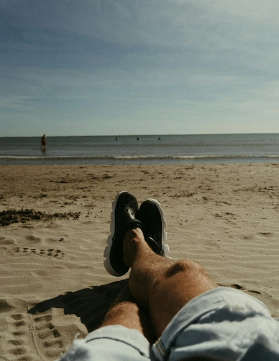 person laying on beach with feet crossed in front of ocean