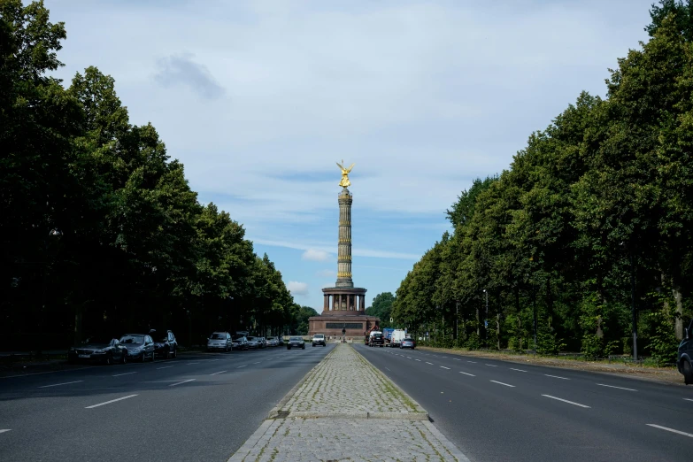 a monument in the middle of a long road with trees on either side