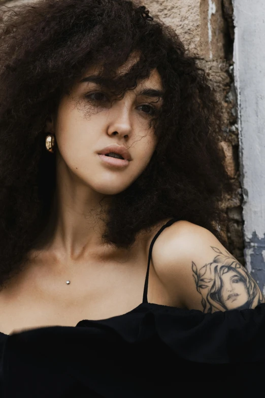 a woman with curly hair posing by a wall