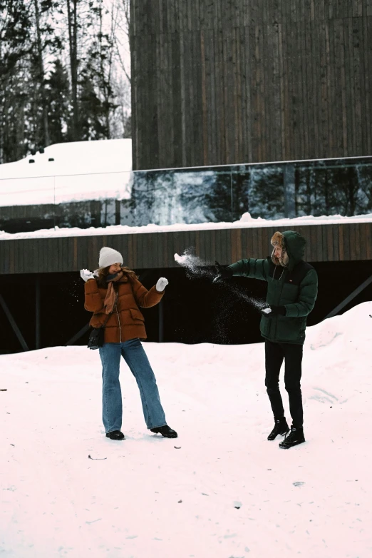 two women standing together in the snow by a building