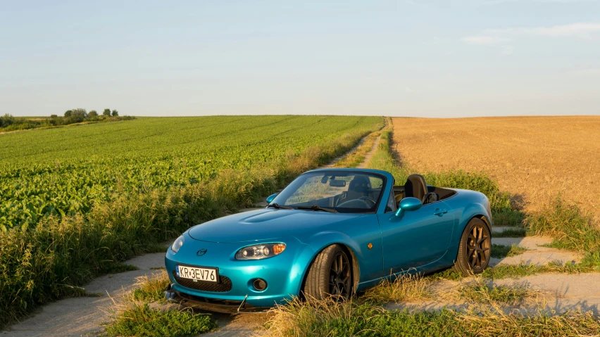 a blue sports car in front of an empty wheat field