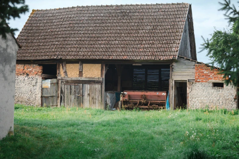 old barn sitting in grass next to a tree