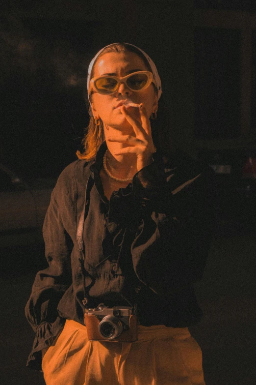 a woman smoking and wearing goggles, holding a camera