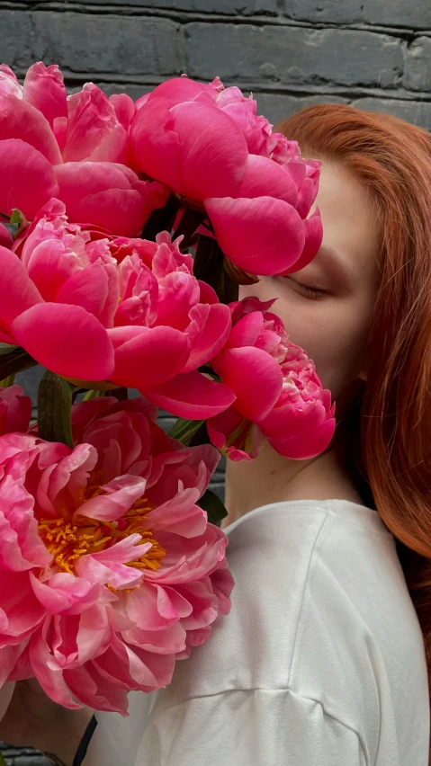 a woman in white shirt kissing pink flowers