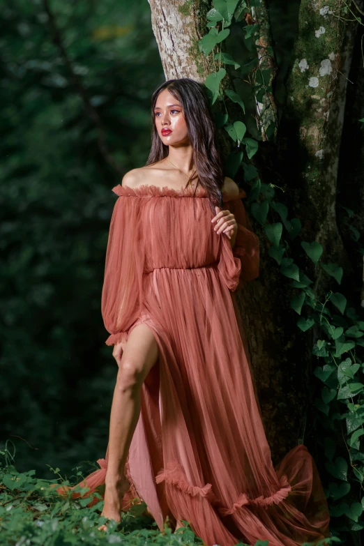 woman in an off shoulder dress standing next to tree