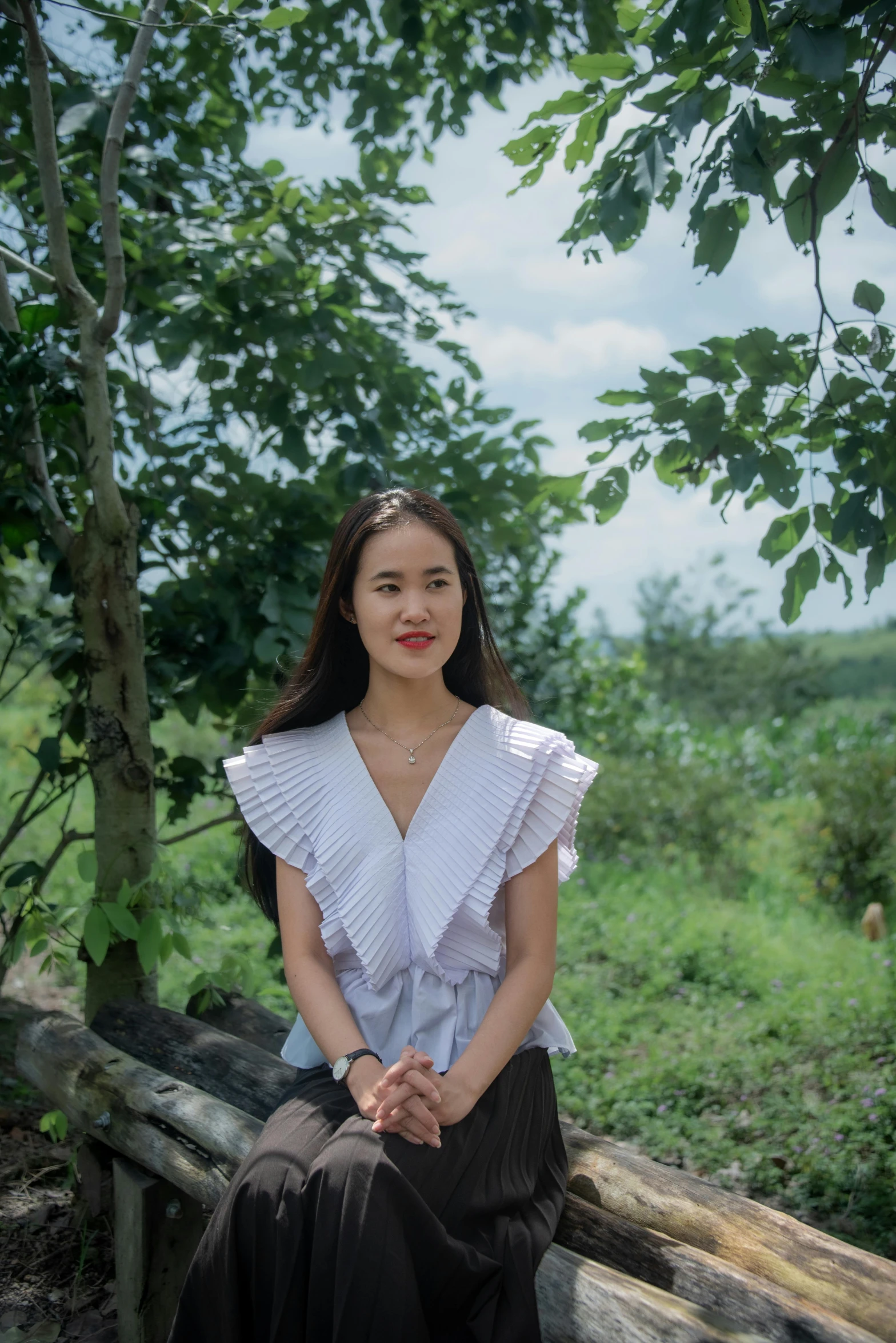 a woman in a white top and black skirt sitting on a tree trunk