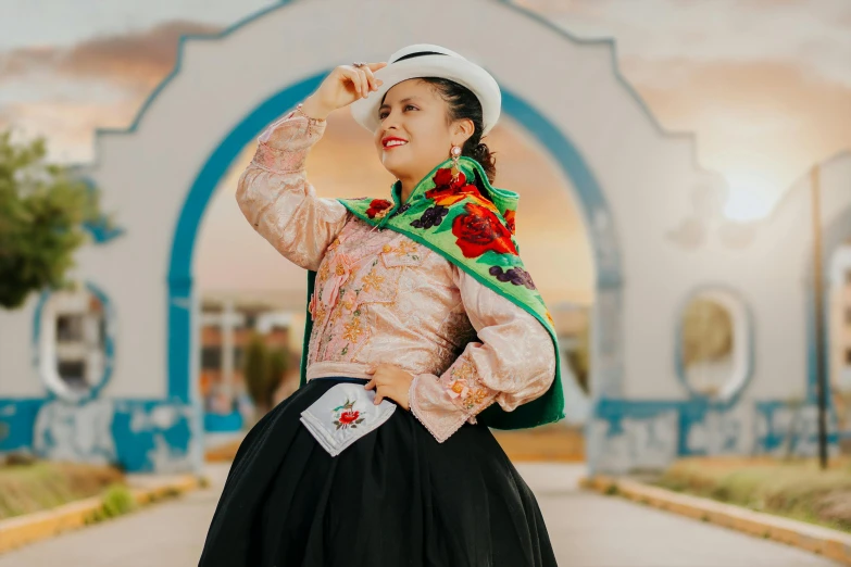 woman in dress and white hat posing in front of an arch