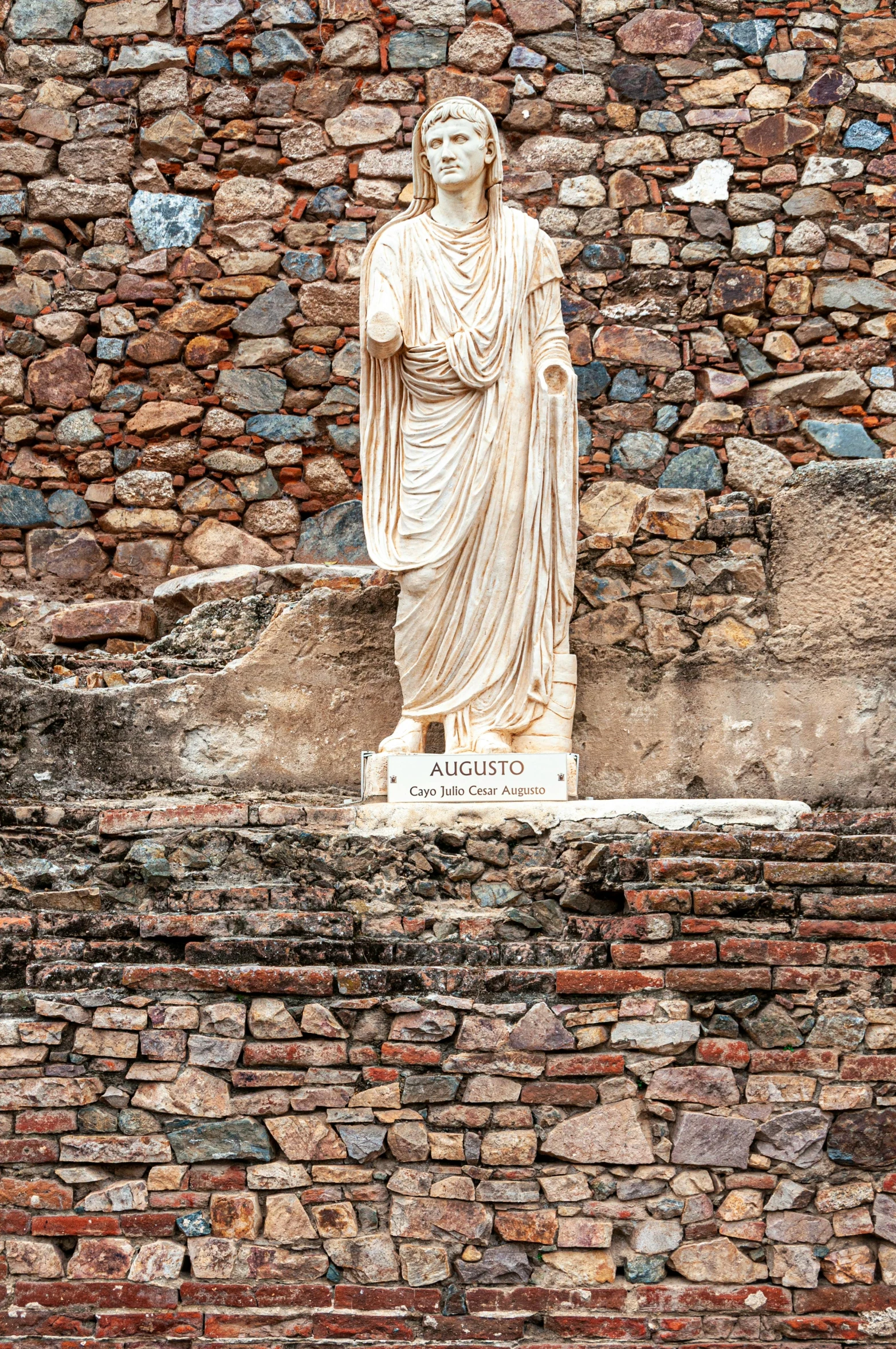 the statue stands in front of a wall that has a large stone sculpture of a woman on it