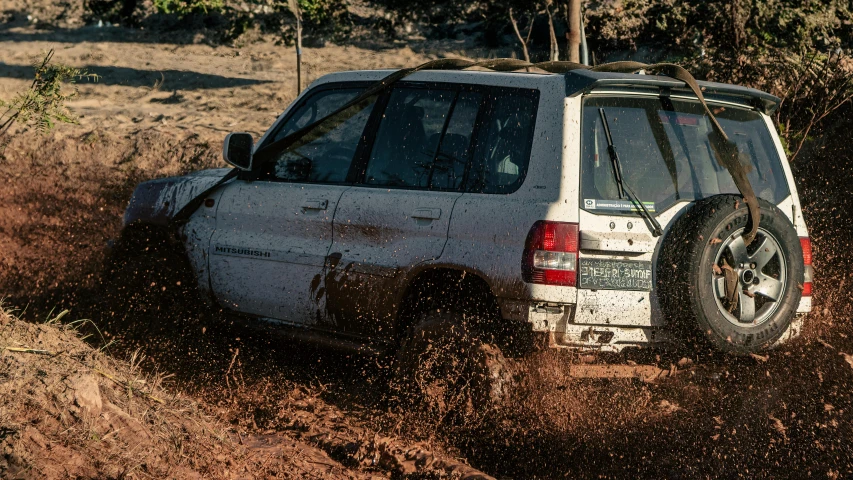 a white suv driving through dirt with trees in the background